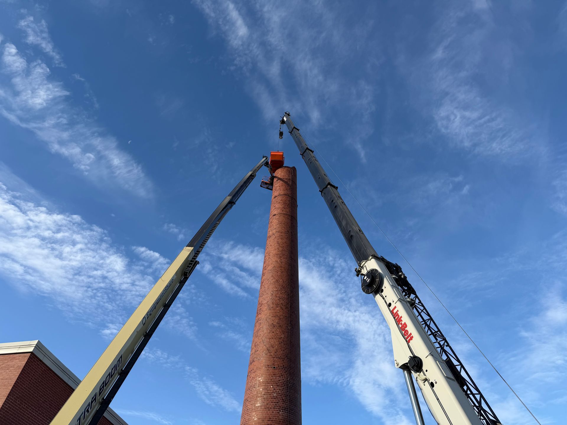 CL Construction crew performing hand demolition on a tall industrial smokestack at the Lincoln Regional Center site in Lincoln, Nebraska. Workers use manual tools and safety gear to carefully dismantle sections of the 143-foot chimney structure amid rubble and heavy equipment on the ground