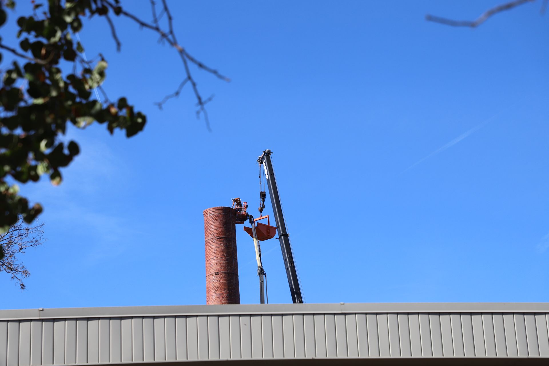 CL Construction crew performing hand demolition on a tall industrial smokestack at the Lincoln Regional Center site in Lincoln, Nebraska. Workers use manual tools and safety gear to carefully dismantle sections of the 143-foot chimney structure amid rubble and heavy equipment on the ground