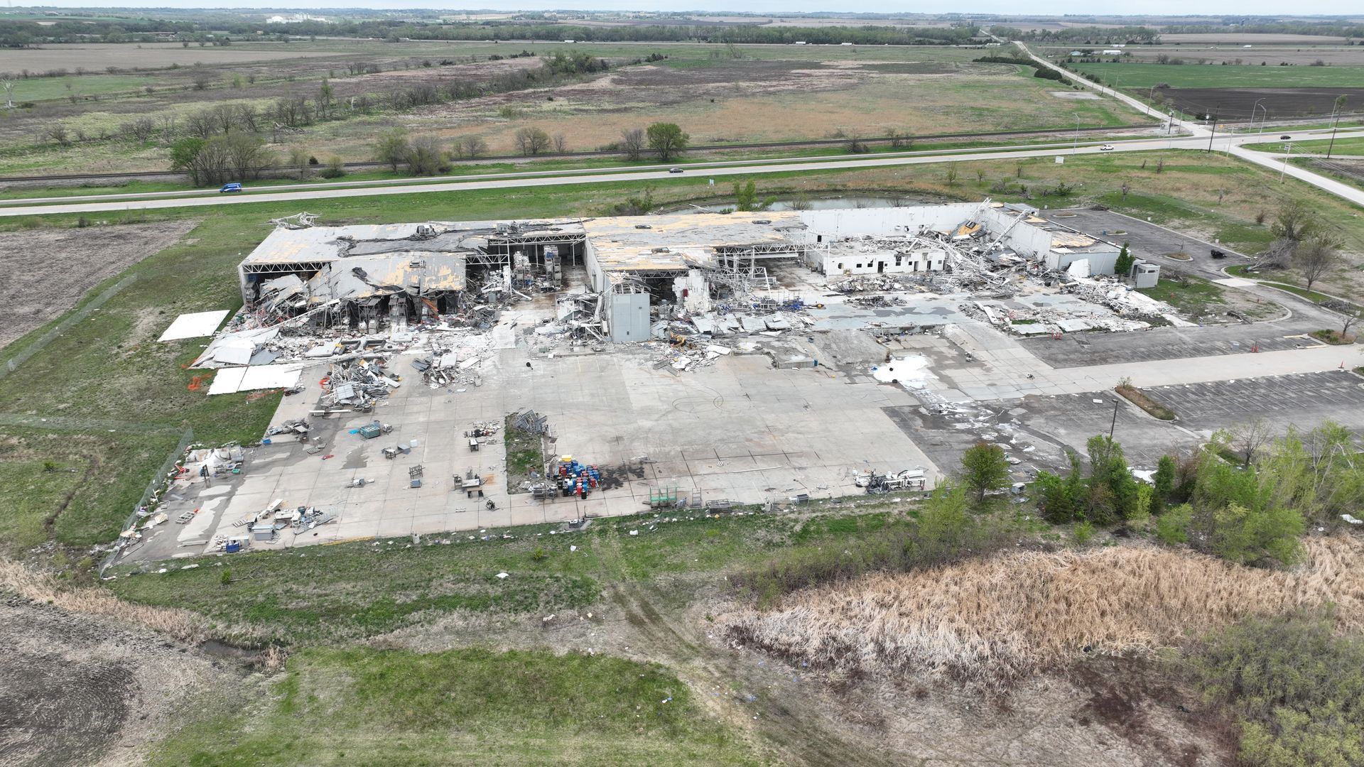 Aerial view of a damaged industrial building surrounded by debris and rural fields.
