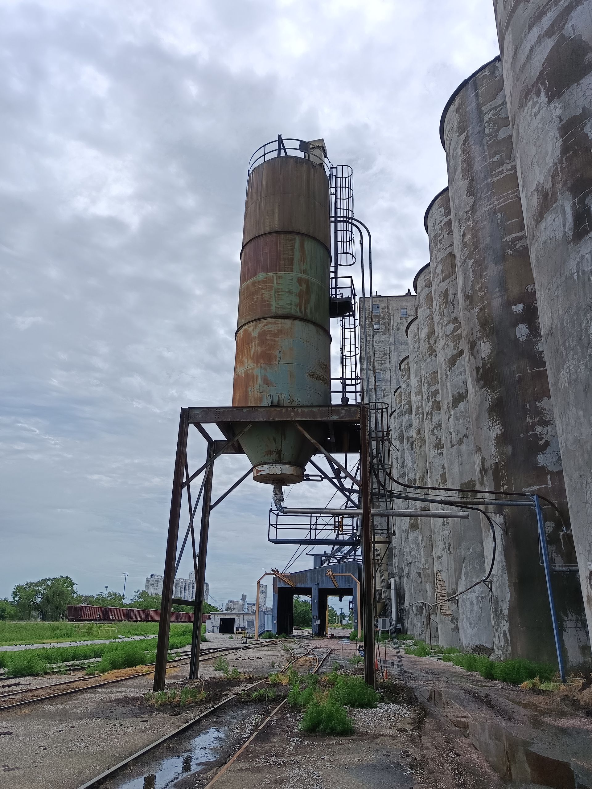 A large rusty silo is sitting in front of a large building.