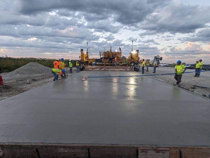 A group of construction workers are working on a concrete road.