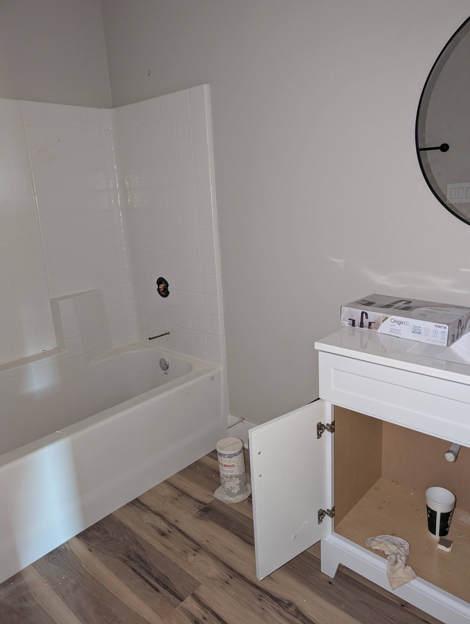 Bathroom under renovation with white tub, open vanity cabinet, and round mirror on the wall