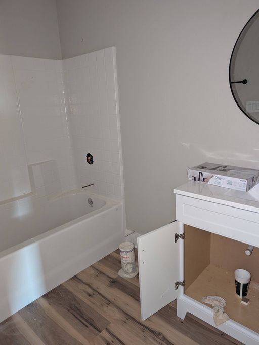 Bathroom under renovation with white tub, open vanity cabinet, and round mirror on the wall