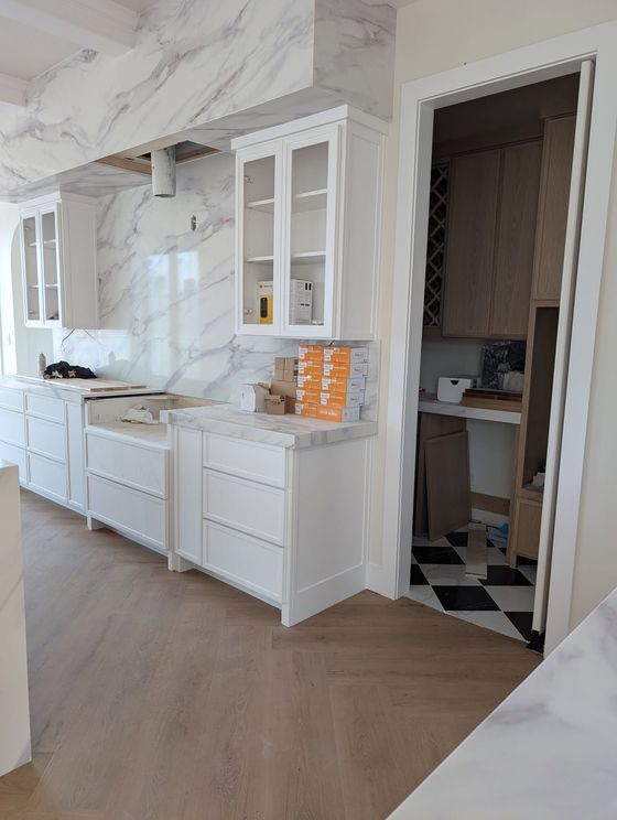 Bright white kitchen with marble-look surfaces, built-in cabinets, and a doorway to a patterned tiled room