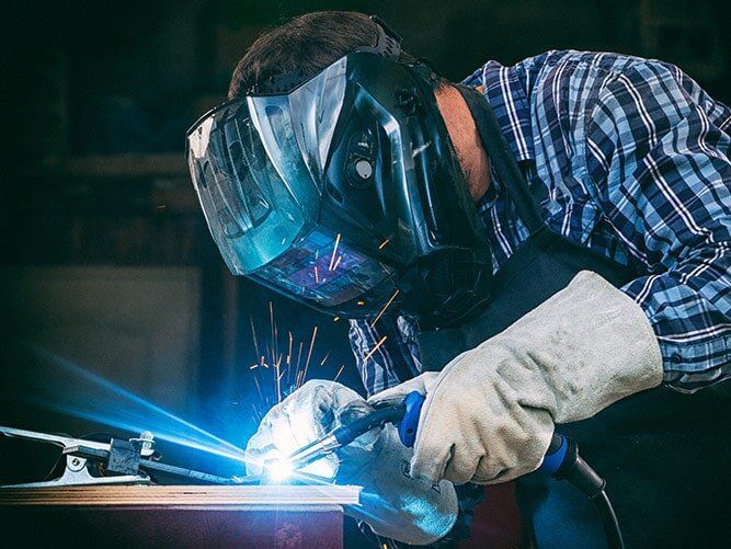 A Man Wearing a Welding Mask and Gloves is Welding a Piece of Metal — Sun City Sheetmetal In Garbutt, QLD