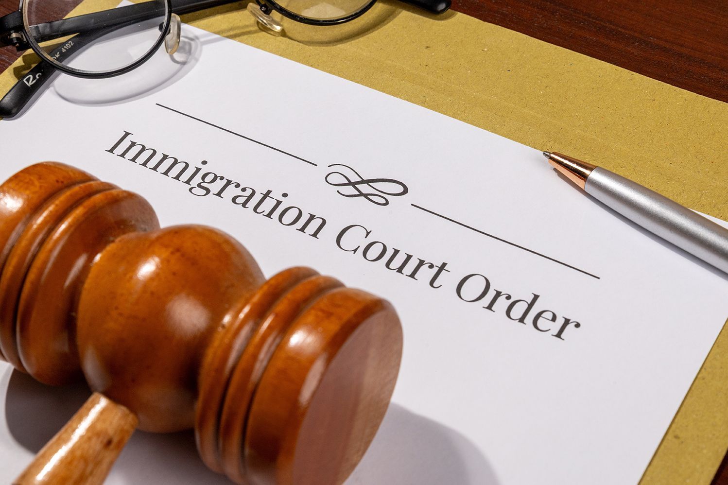 Wooden gavel on Immigration Court Order document, with glasses and pen.