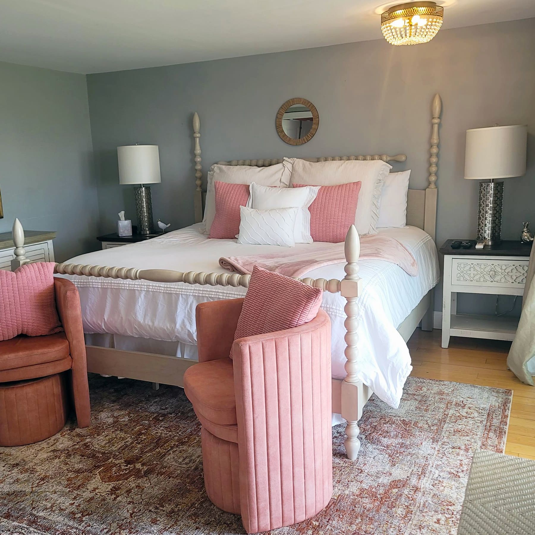 Bedroom with a light-colored bed, pink accents, two chairs, and a patterned rug on a wooden floor.