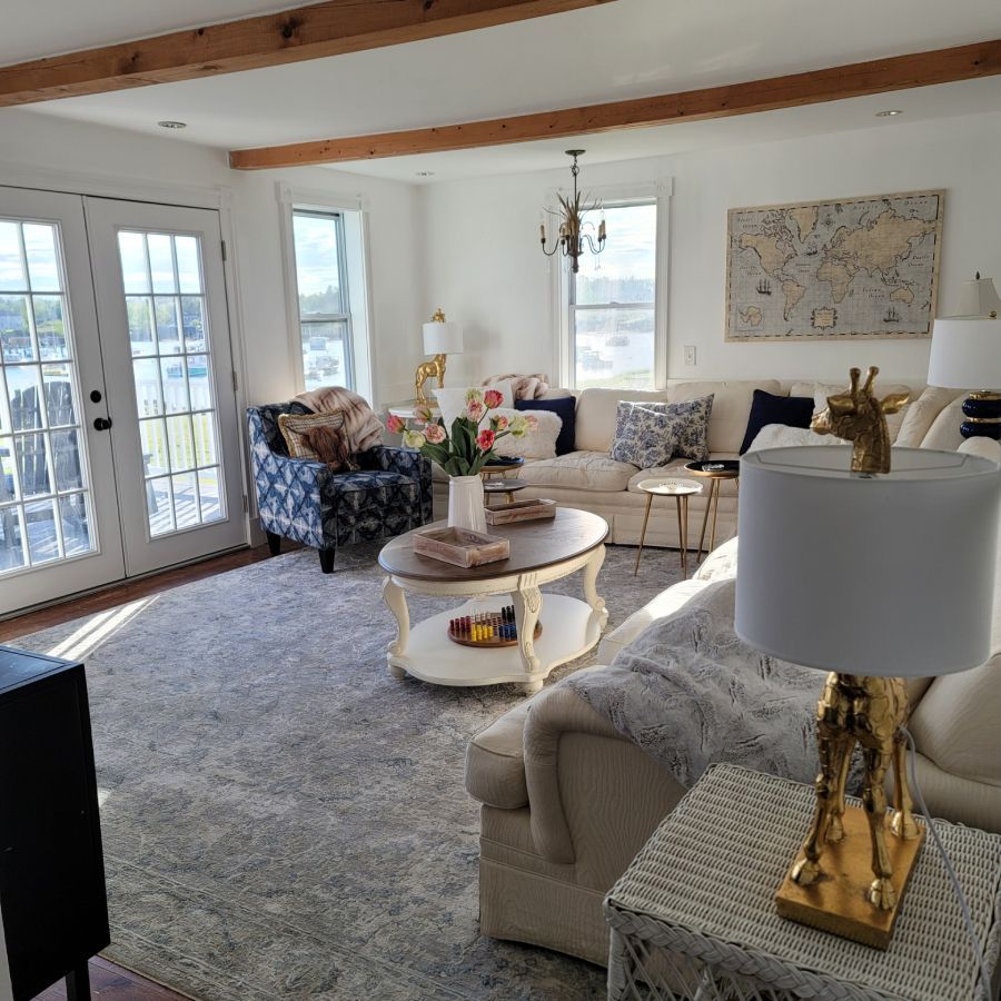 Living room with cream couches, patterned chair, rug, French doors, and exposed wooden beams.