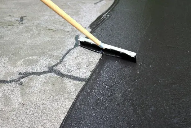 A person sealcoating asphalt. A person is spreading asphalt on a concrete surface to seal coat it.