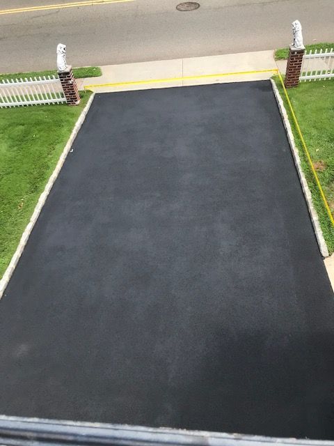 A black asphalt driveway with a white fence in the background.
