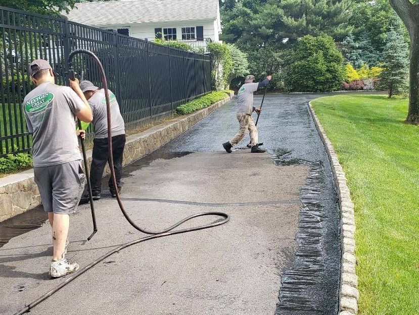 A group of men are cleaning a driveway with a hose.