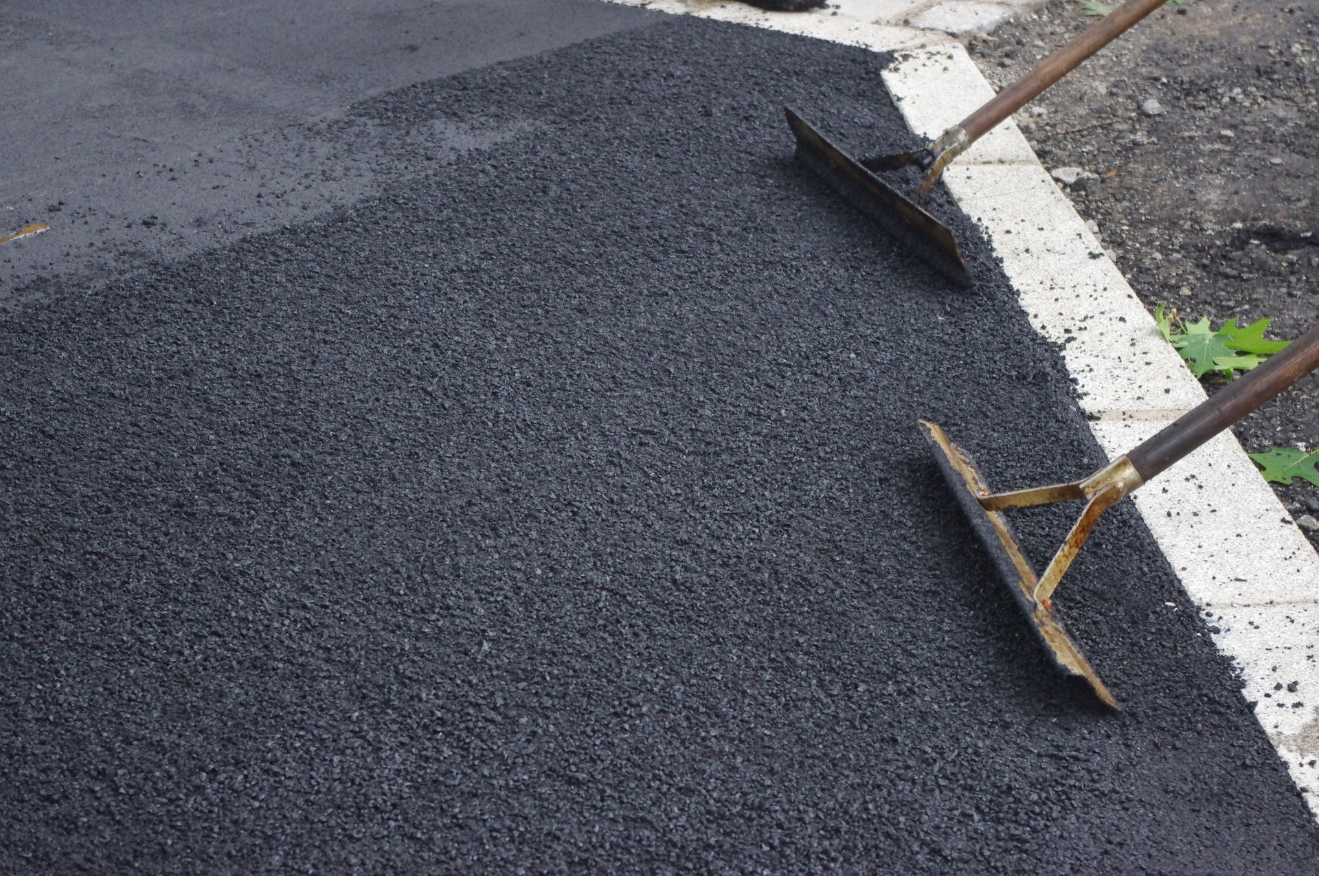 Black asphalt being spread on a road with two shovels beside a white lane line