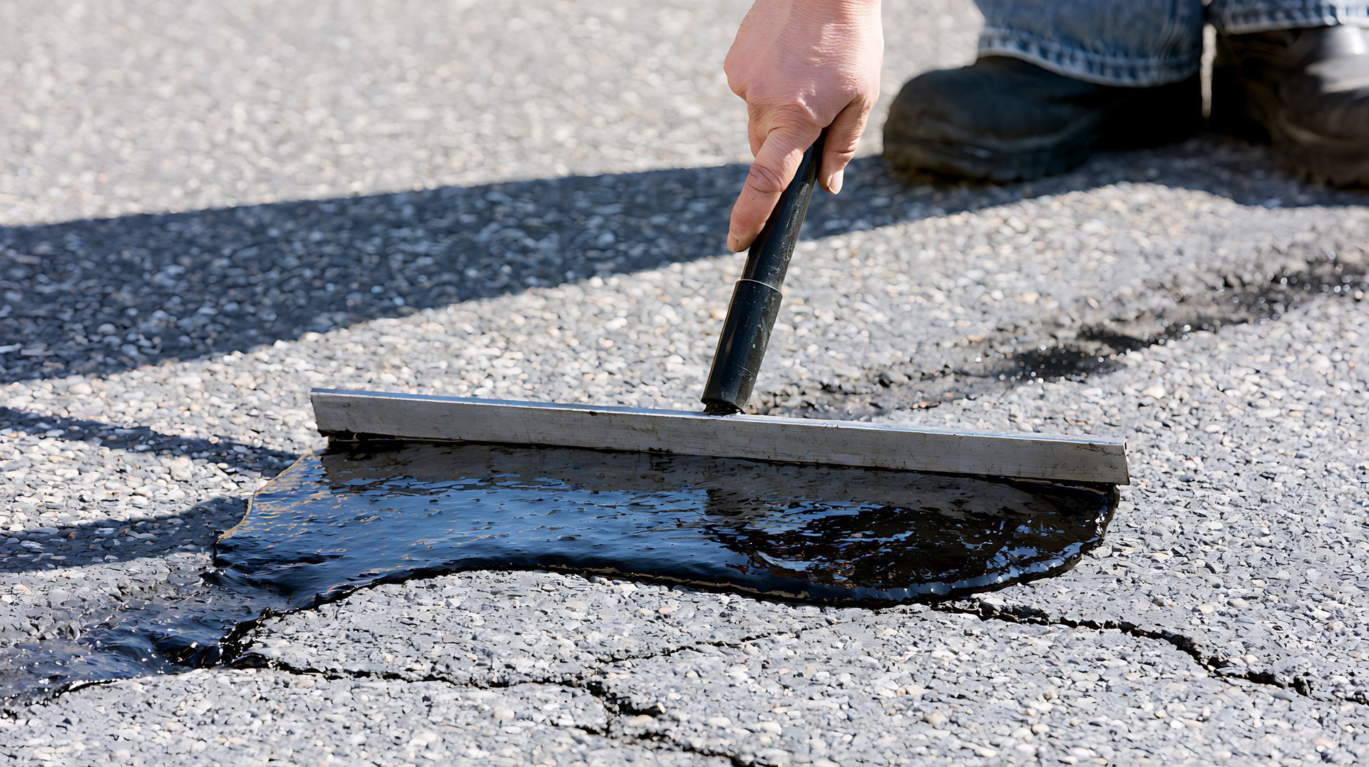 Person spreading black roof sealant over a crack in asphalt with a trowel