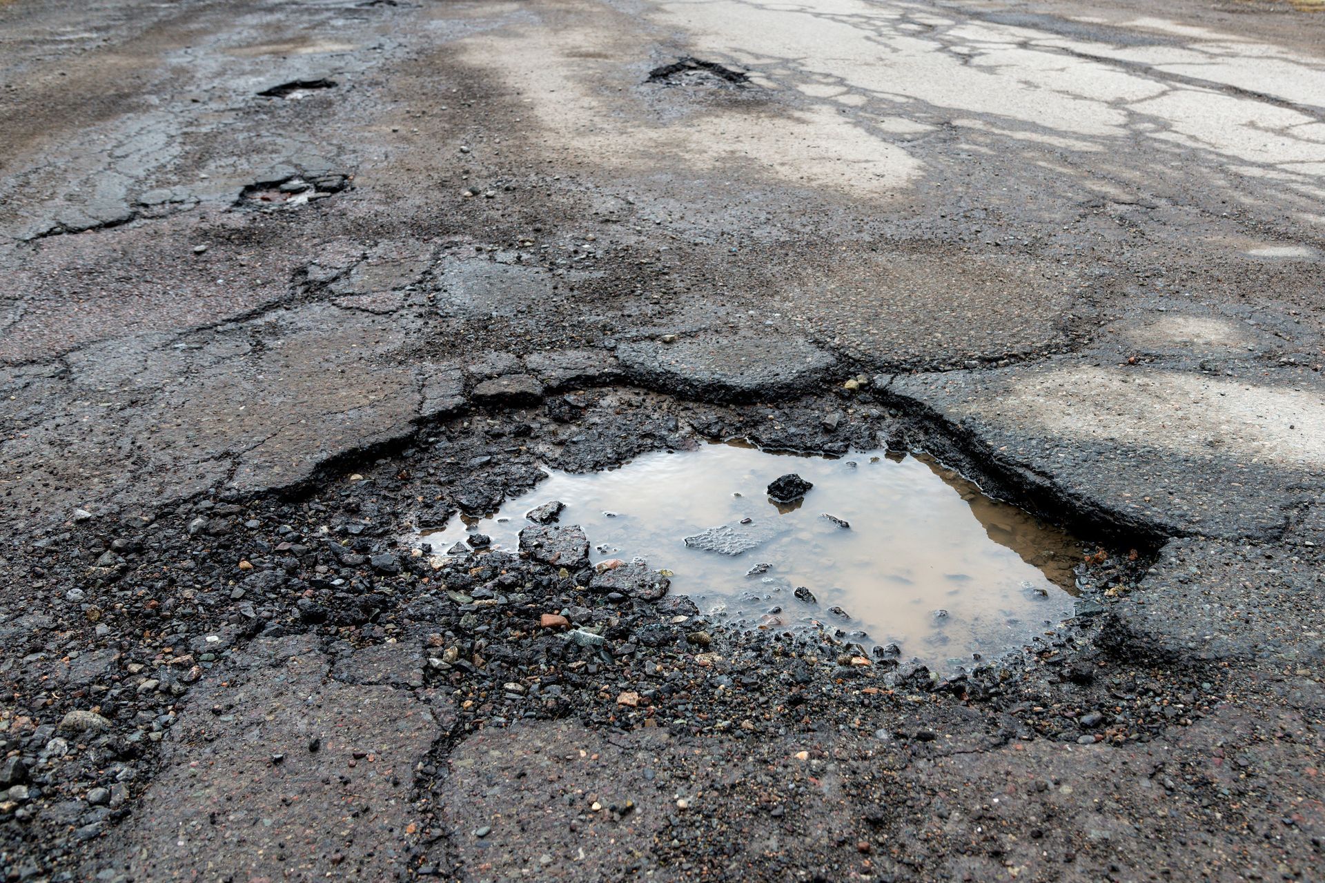 Large pothole filled with water on a cracked, damaged road surface