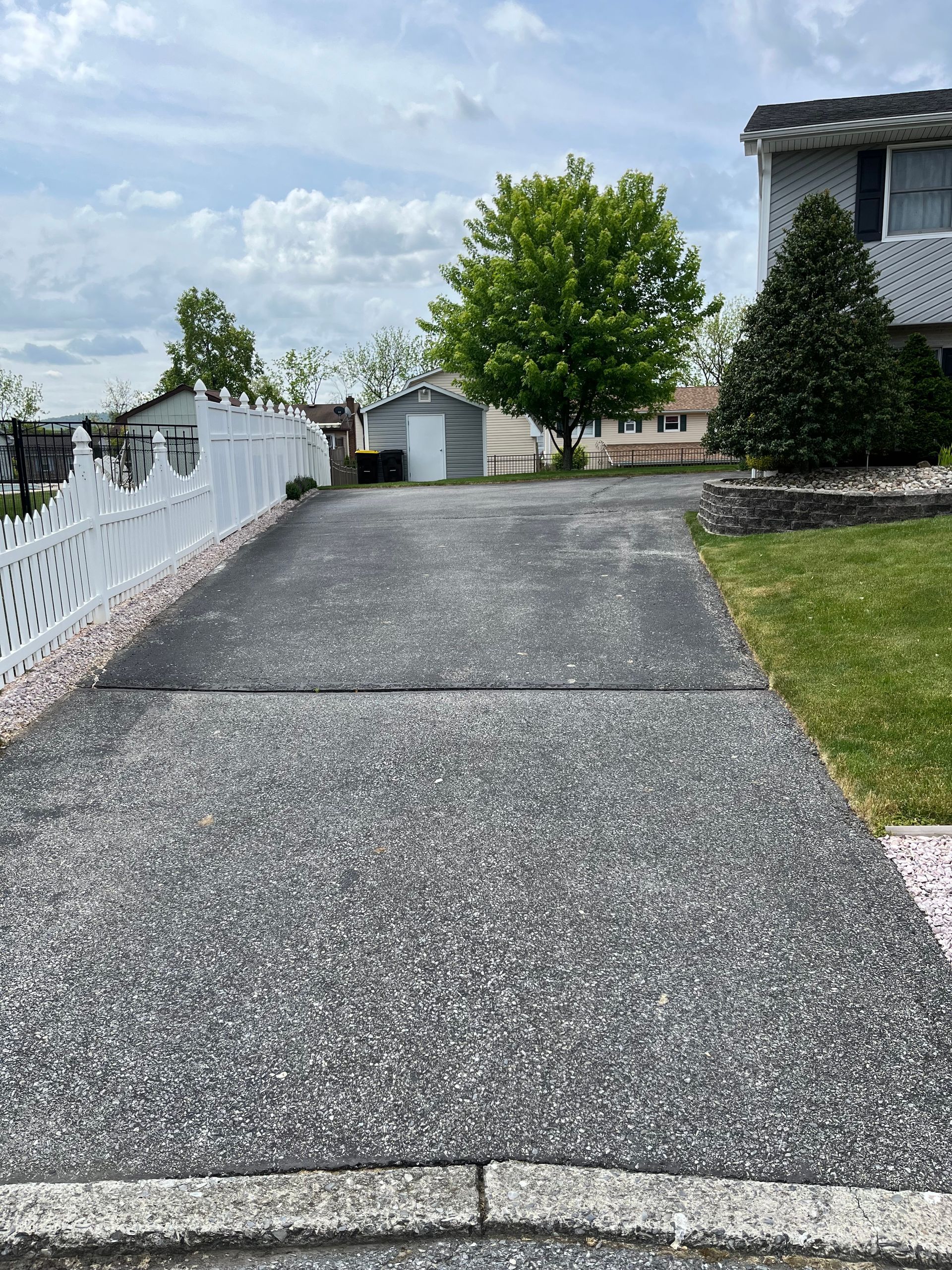 A driveway leading to a house with a white fence.