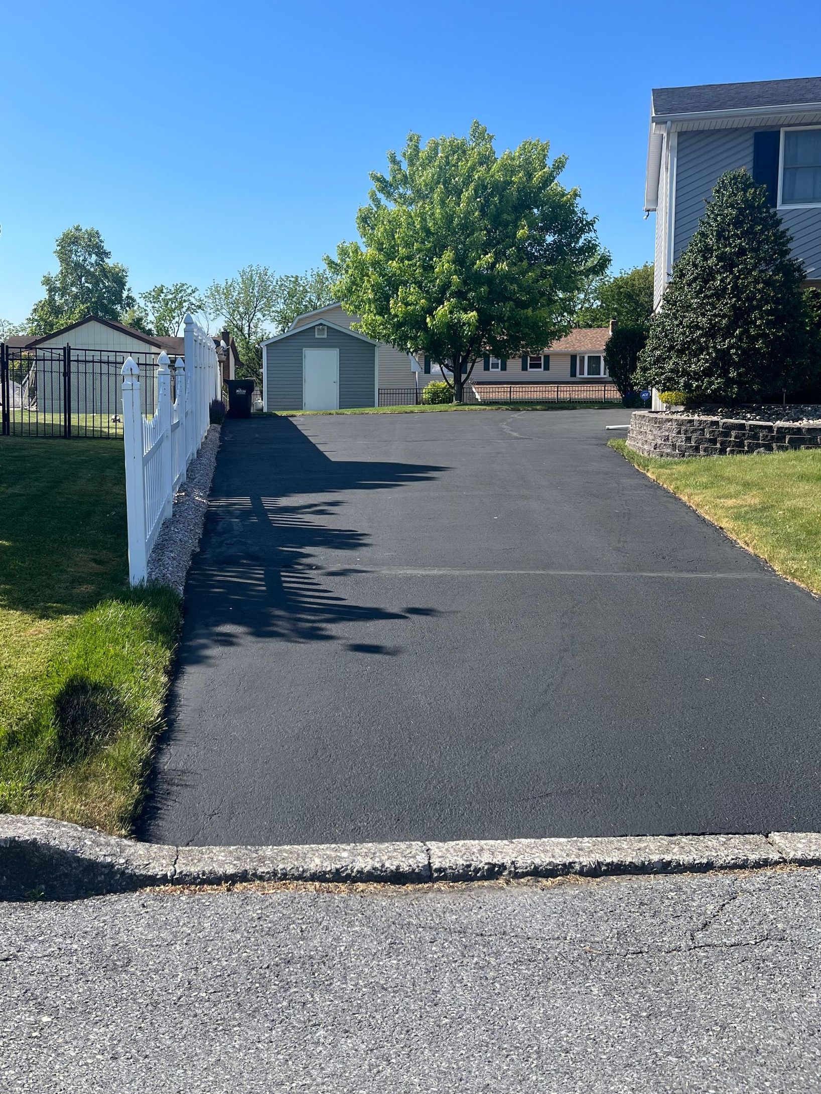 A black driveway leading to a house with a white fence.