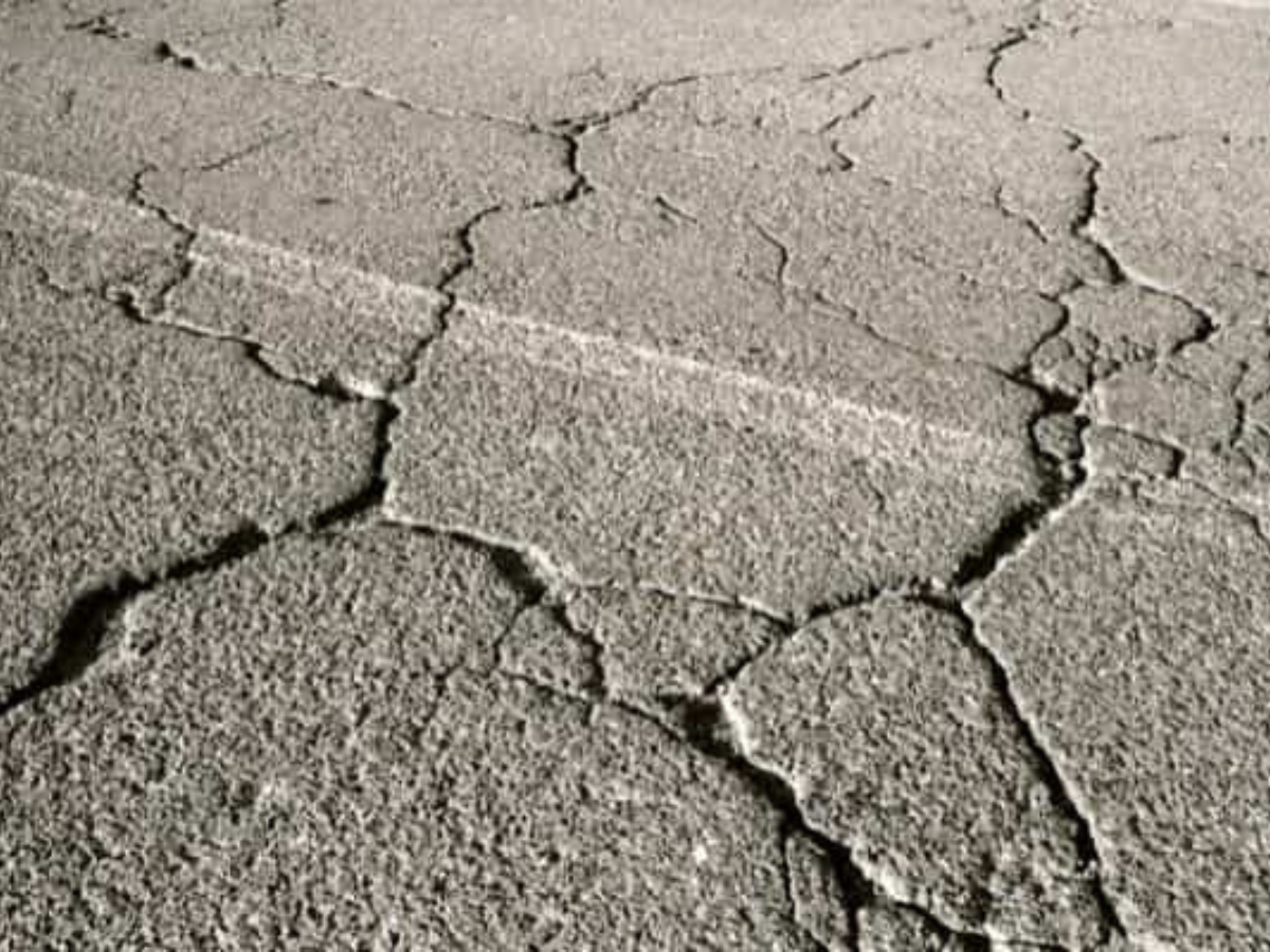 A black and white photo of a cracked asphalt surface.