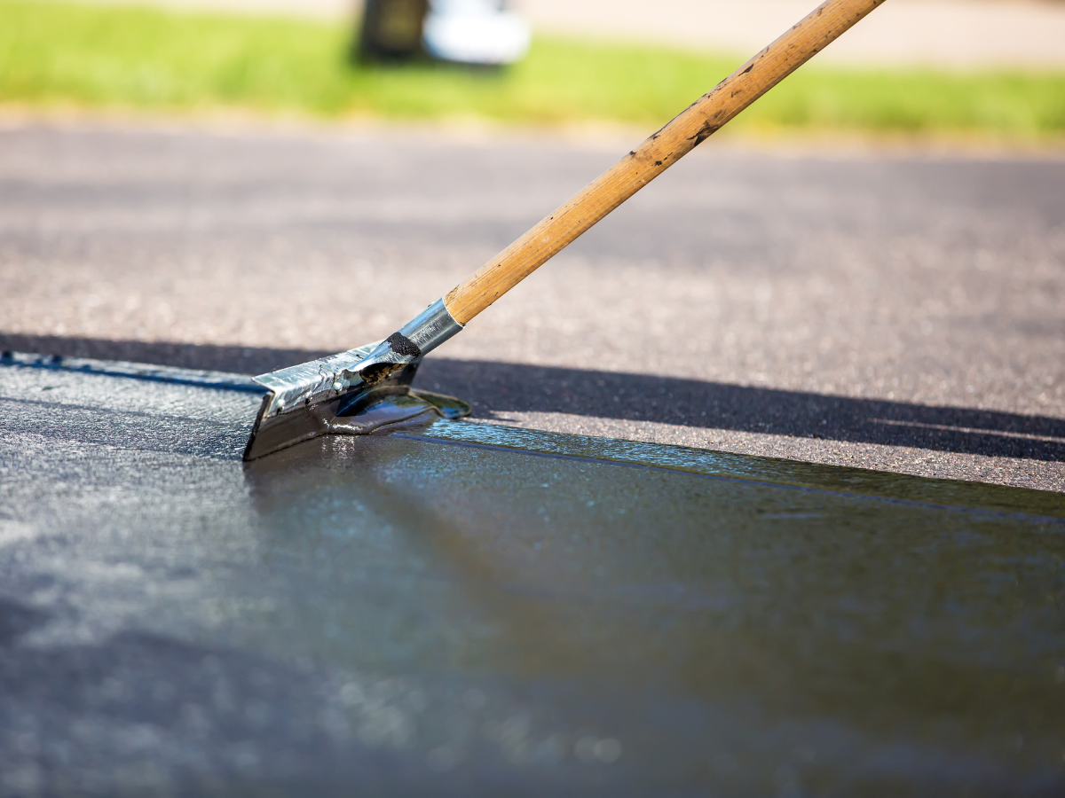 A person is using a broom to spread asphalt on the ground.
