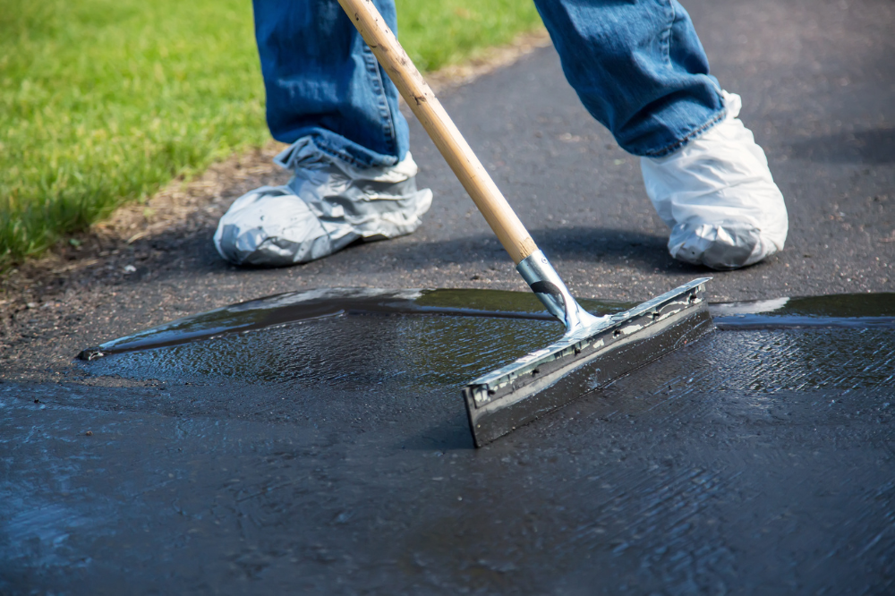 A person is using a broom to spread asphalt on a driveway.
