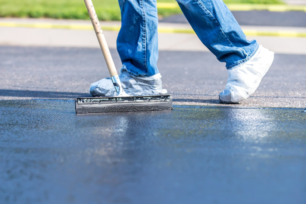 A person is using a broom to spread asphalt on the ground.