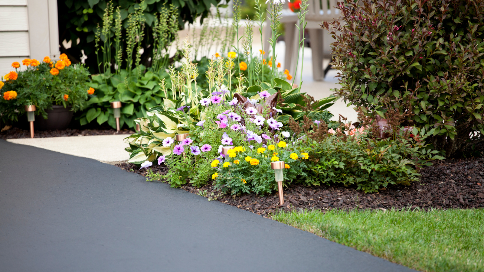 A driveway with flowers on the side of it and a patio in the background.