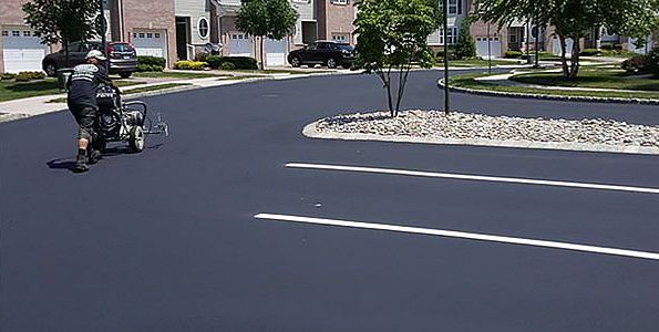 A man is painting lines on the road in a parking lot.