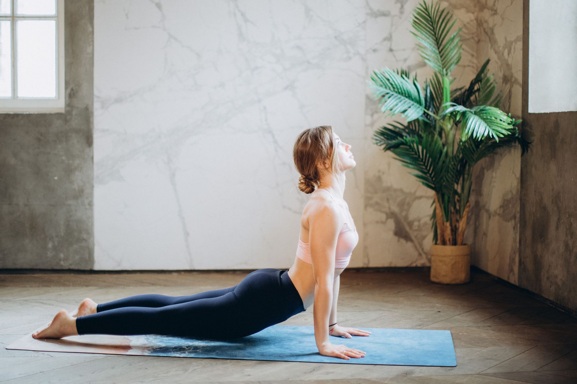 Woman practicing yoga on a mat near a window and plant