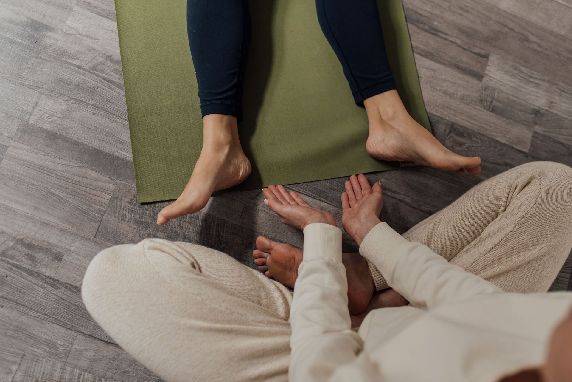 Two people relaxing on yoga mats with feet touching in a stretch