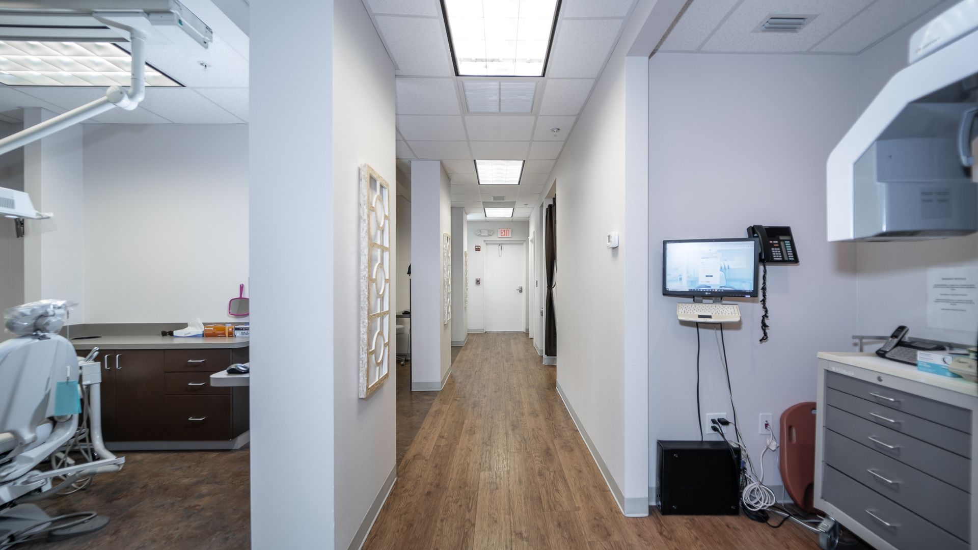 A long hallway in a dental office with a dental chair and a monitor on the wall.