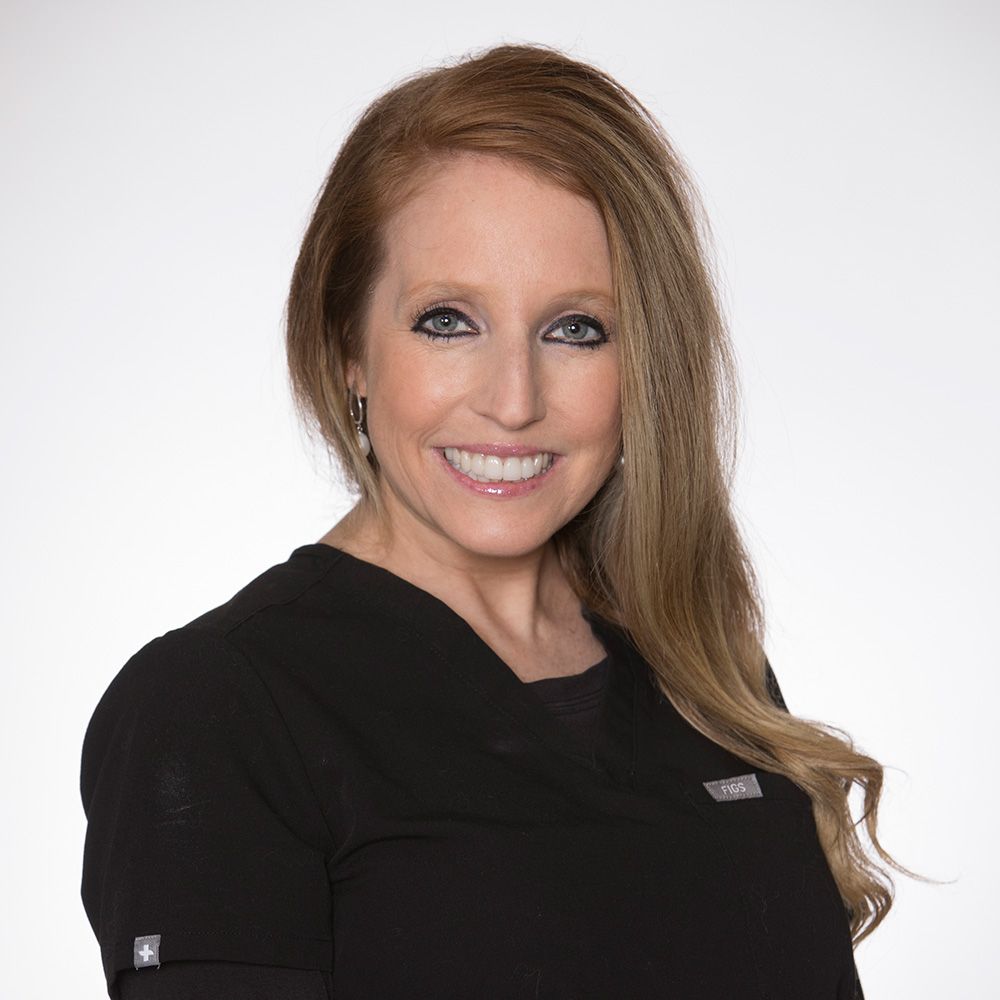A woman wearing a black scrub top is smiling for the camera.