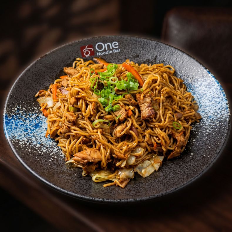 Plate of stir-fried noodles topped with chopped green onions on a dark speckled dish