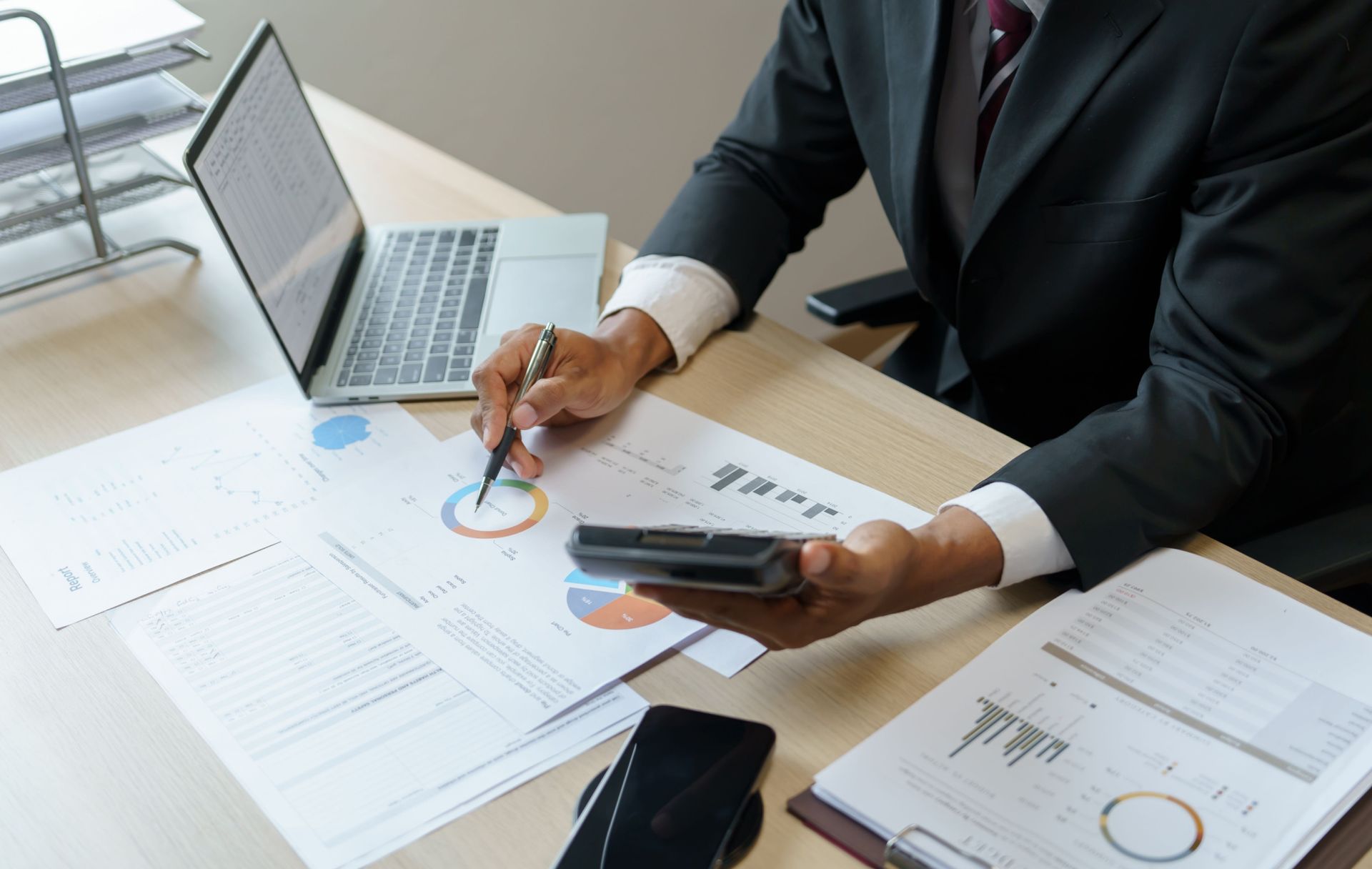 Businessman+analyzing+investment+charts+Invoice+and+pressing+calculator+buttons+over+documents