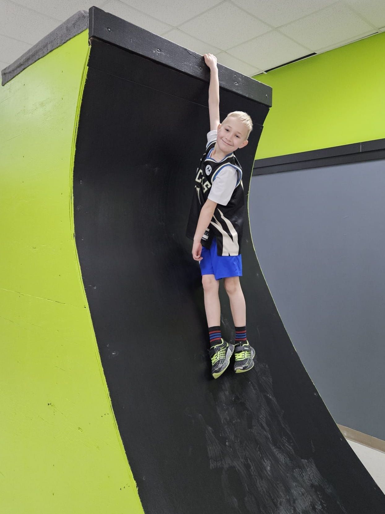 A young boy in an orange shirt is climbing a rope