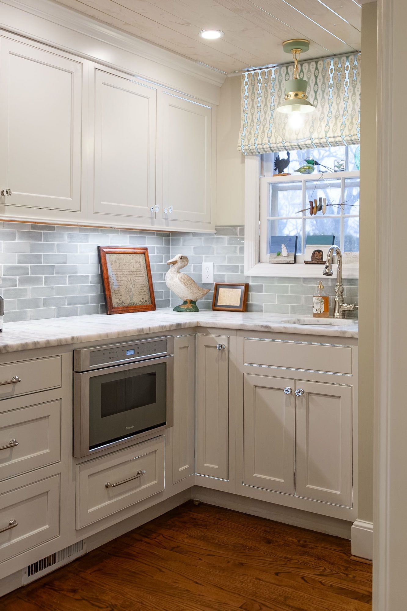 White kitchen with blue tile backsplash and wooden floor. Corner cabinet with built-in microwave.