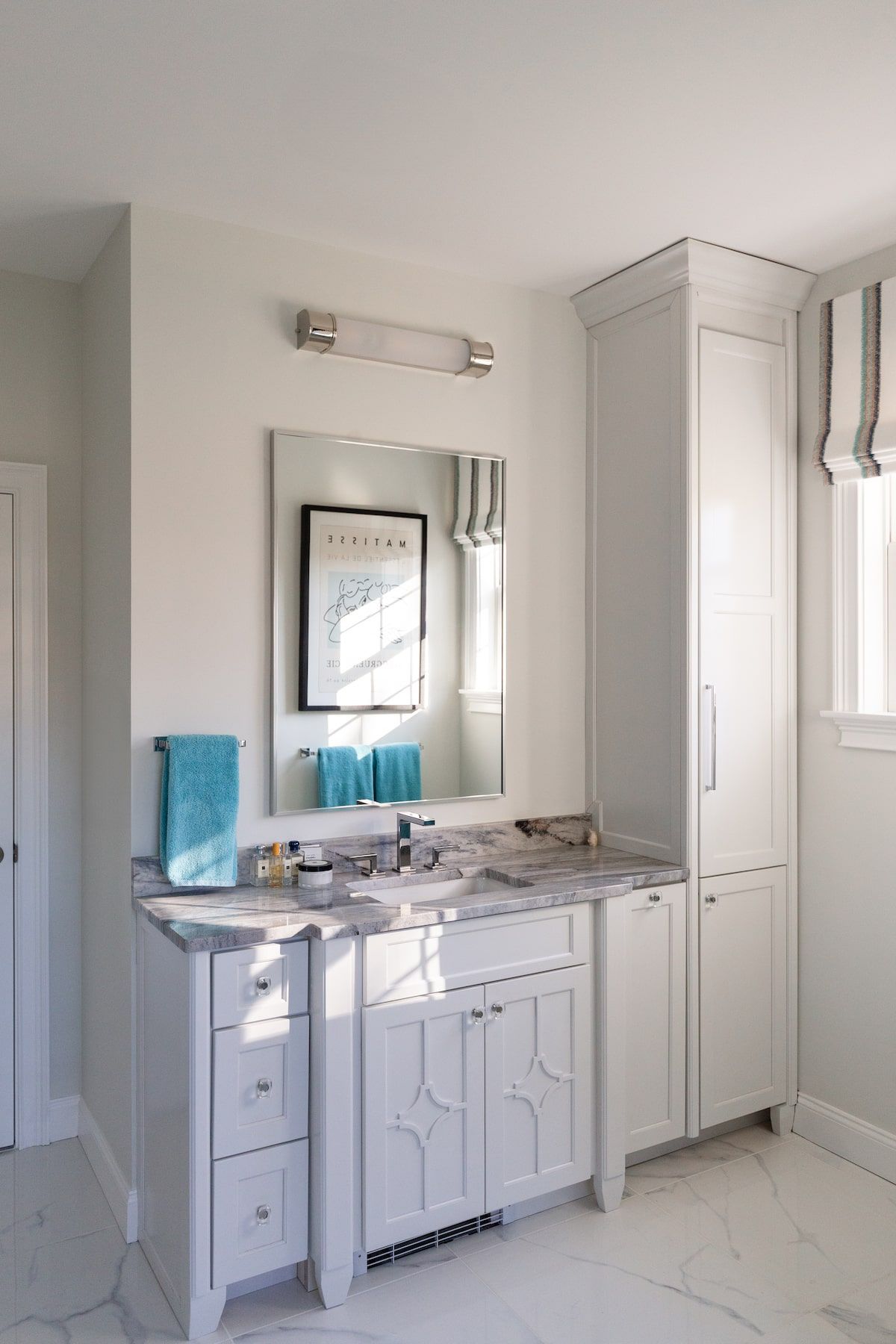 White bathroom with vanity, mirror, and tall cabinet. Turquoise towels. Soft, natural light.