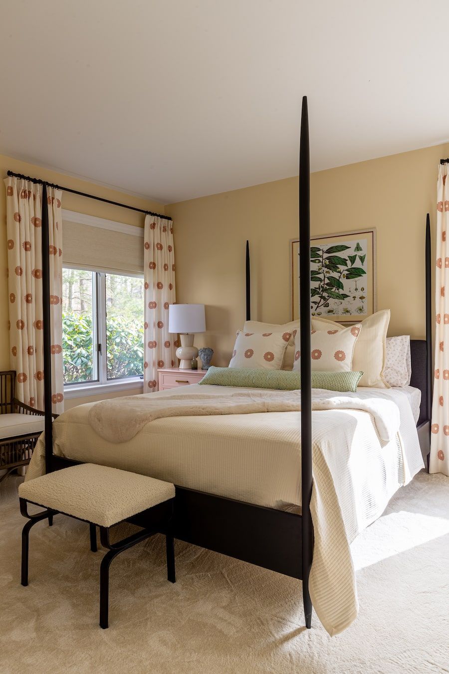 Bedroom with a black canopy bed, white bedding, and patterned curtains; natural light.