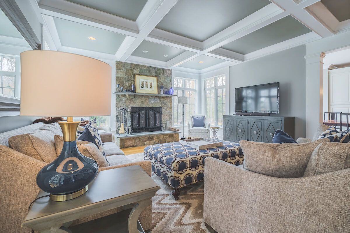 Living room with stone fireplace, coffered ceiling, and a patterned ottoman.