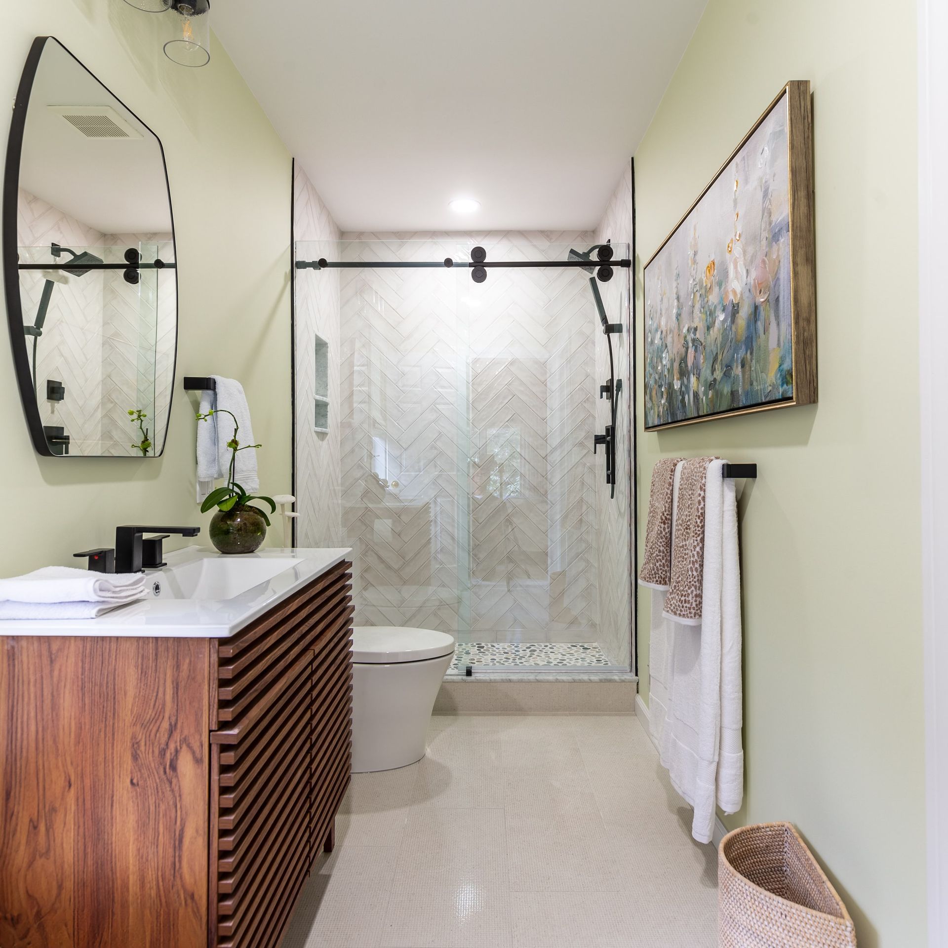 Bathroom with wood vanity, walk-in shower, black fixtures, art, and light green walls.