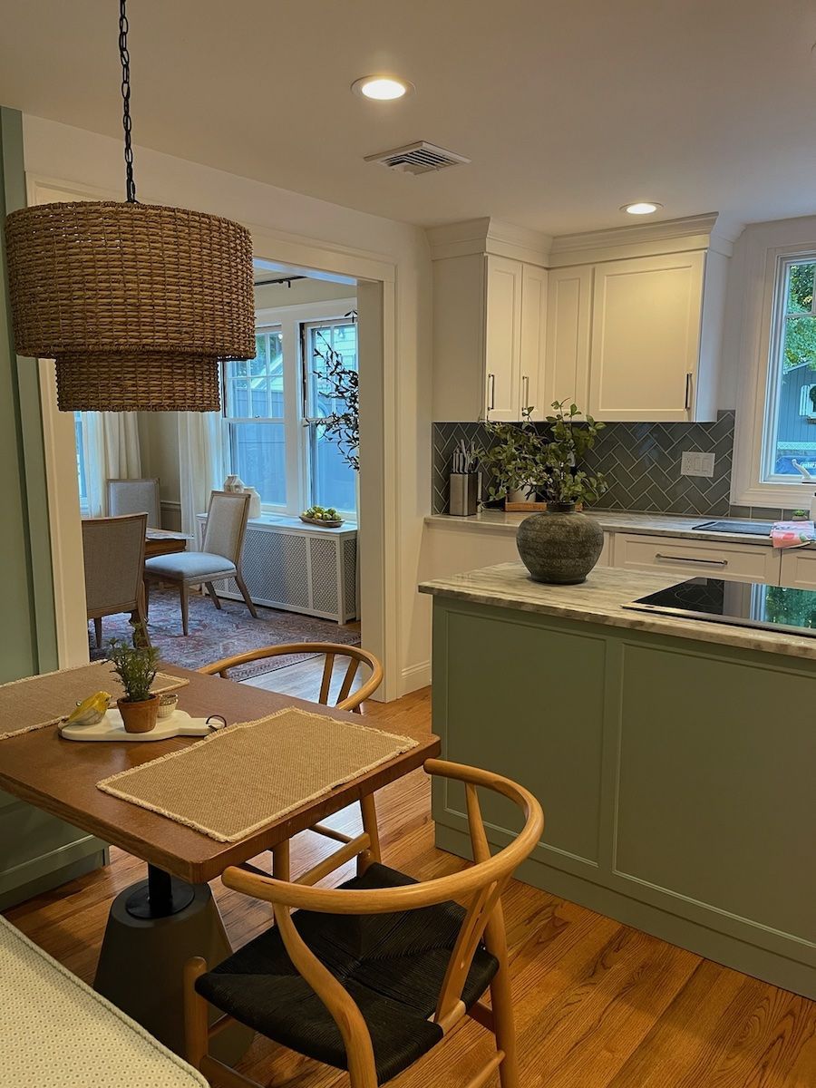 Kitchen with green island, wooden table, wicker light fixture, and view into a dining area.