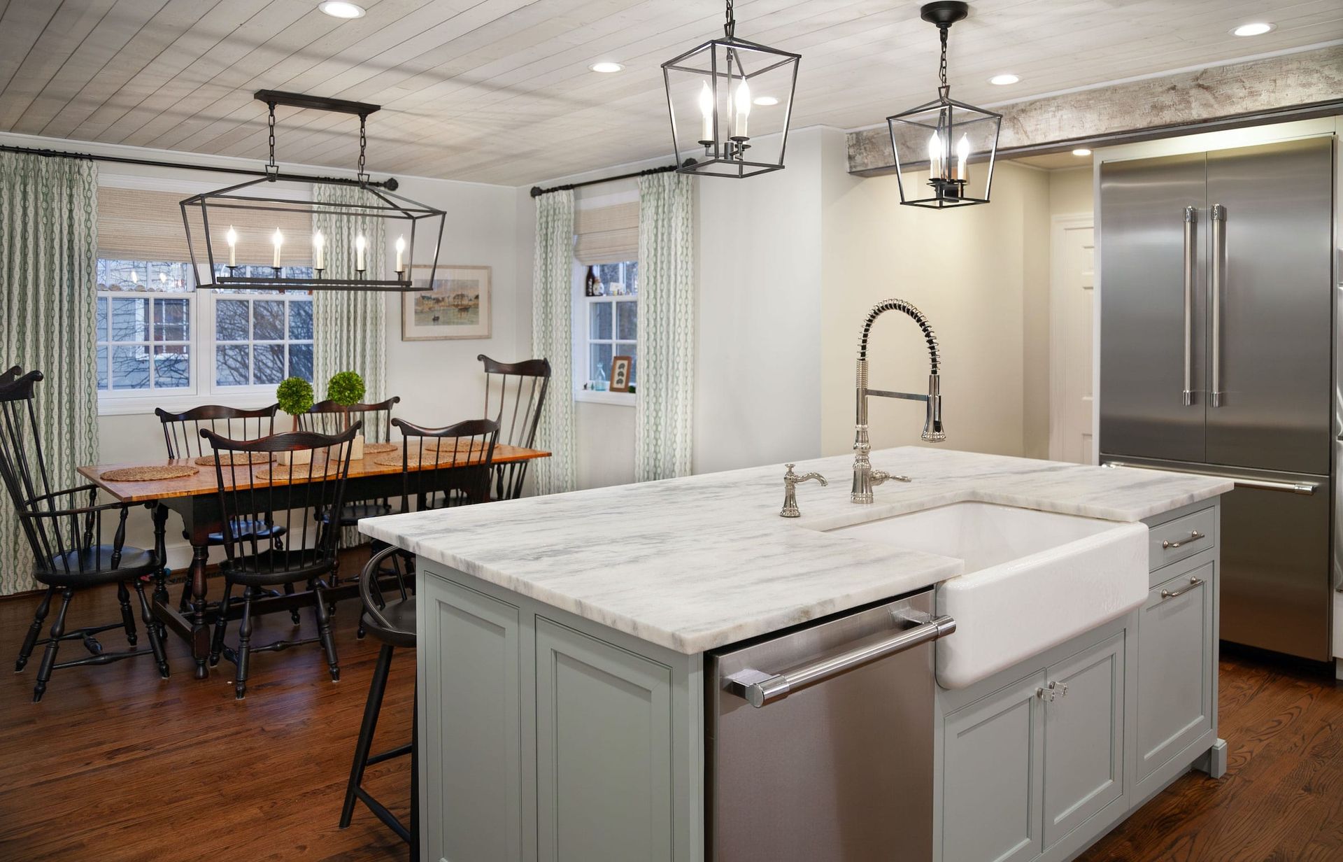 Kitchen with island, farmhouse sink, and dining table. Light blue cabinetry, marble countertops, dark wood floors.