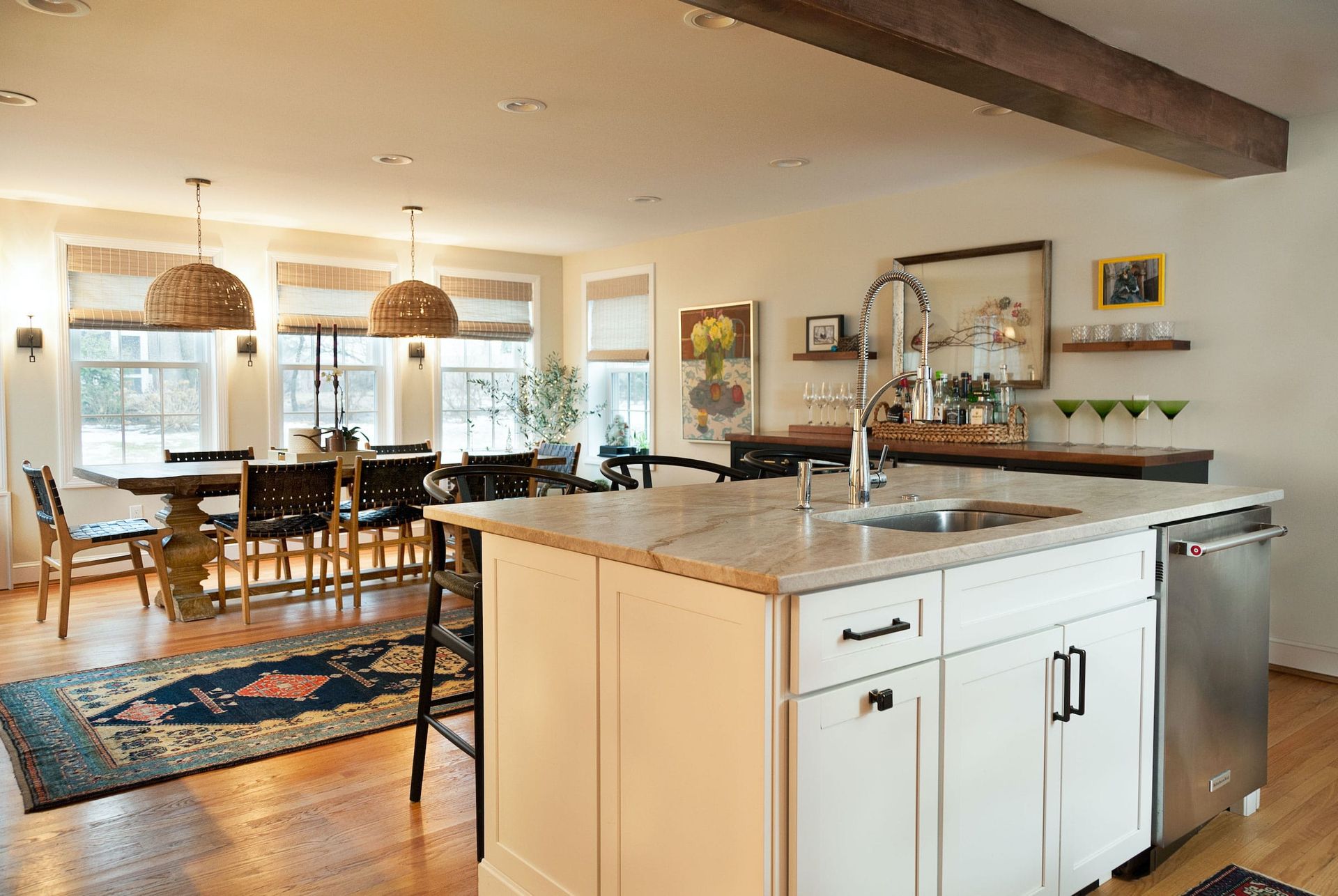 Open-plan kitchen and dining area with island, table, chairs, and windows. Light wood floors and neutral walls.