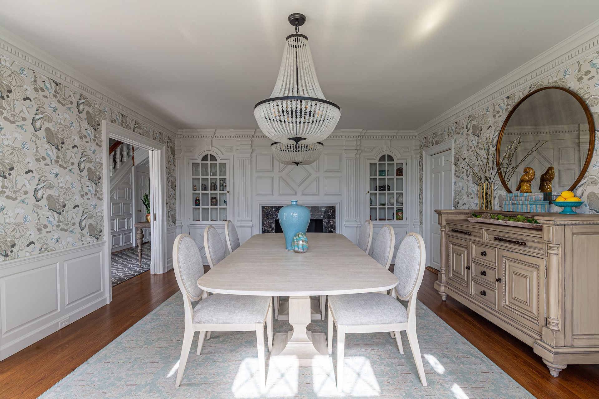Elegant dining room with chandelier, long table, chairs, detailed wallpaper, and ornate buffet.