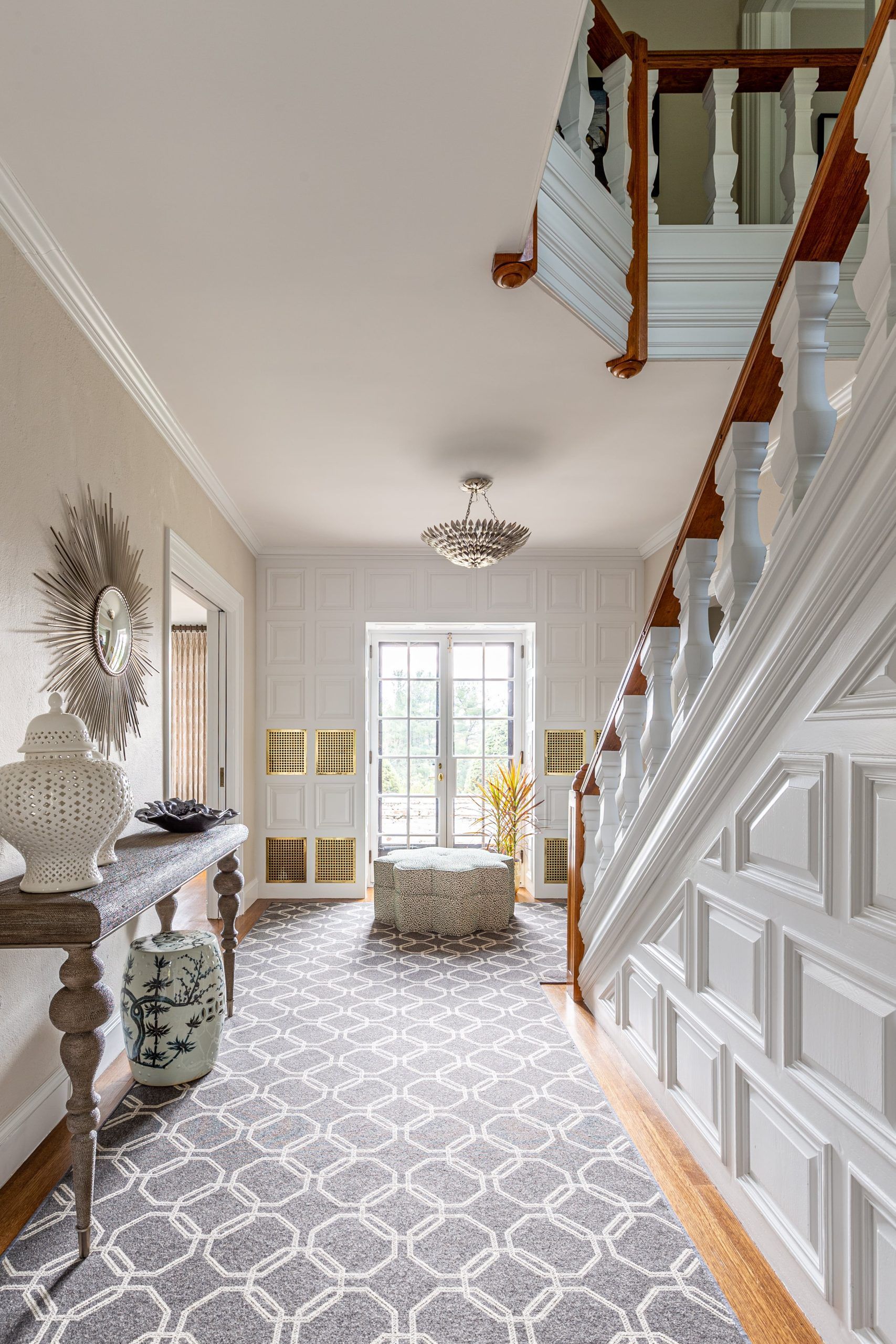 Elegant entryway with a staircase, patterned rug, console table, and a window at the end.