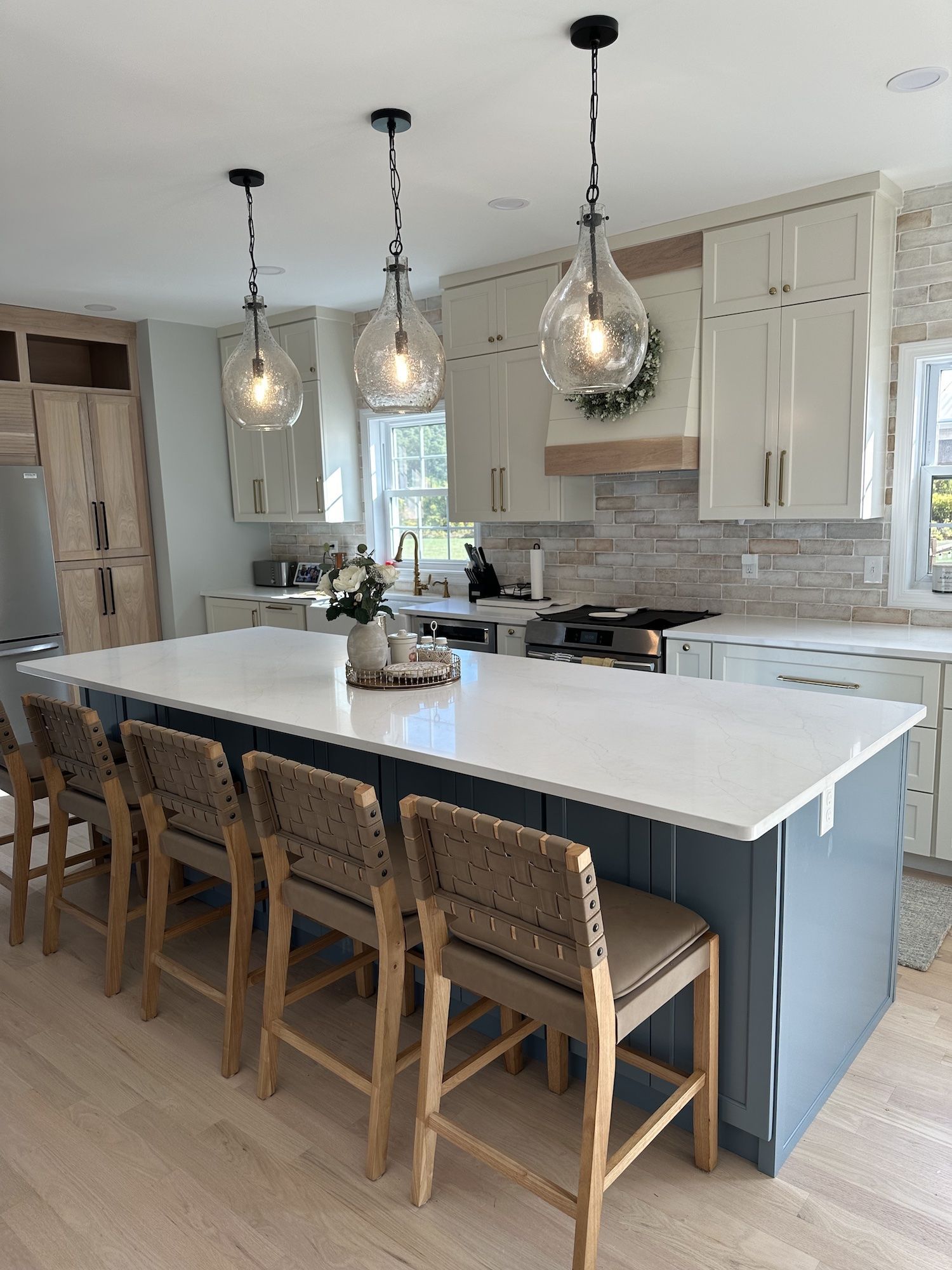Modern kitchen with island and bar stools, pendant lights, light wood and white cabinetry.