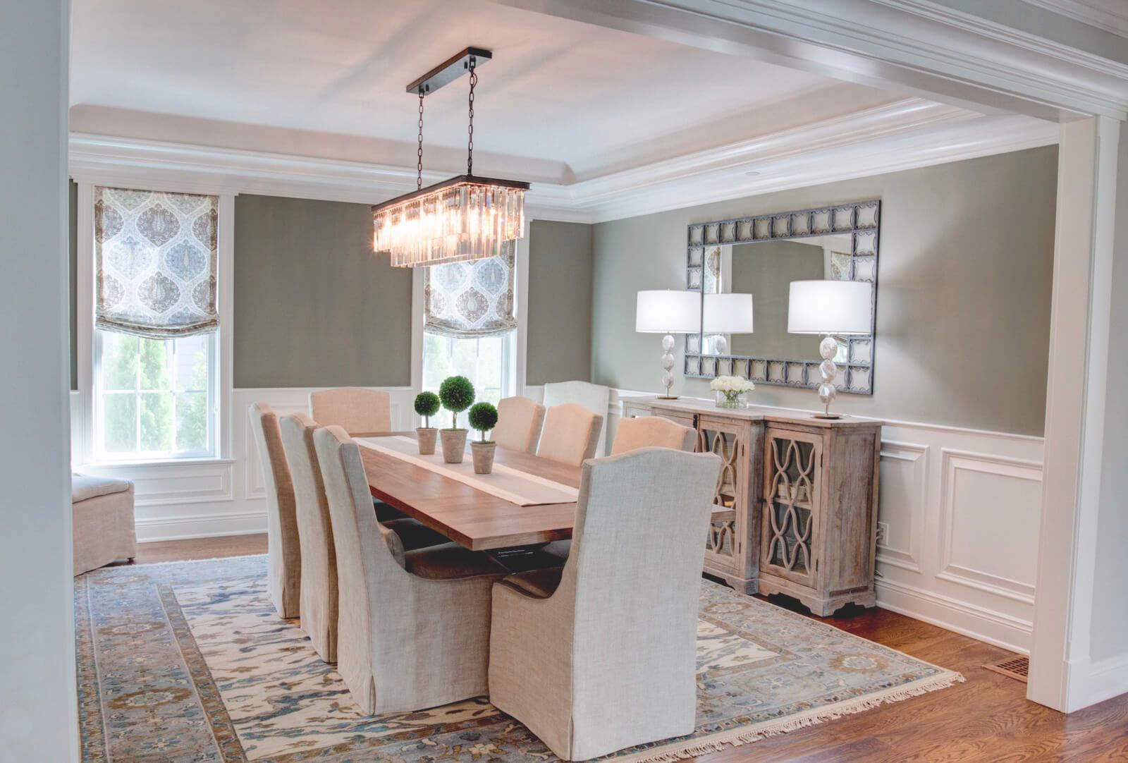 Dining room with a long wooden table, chandelier, and sage green walls.
