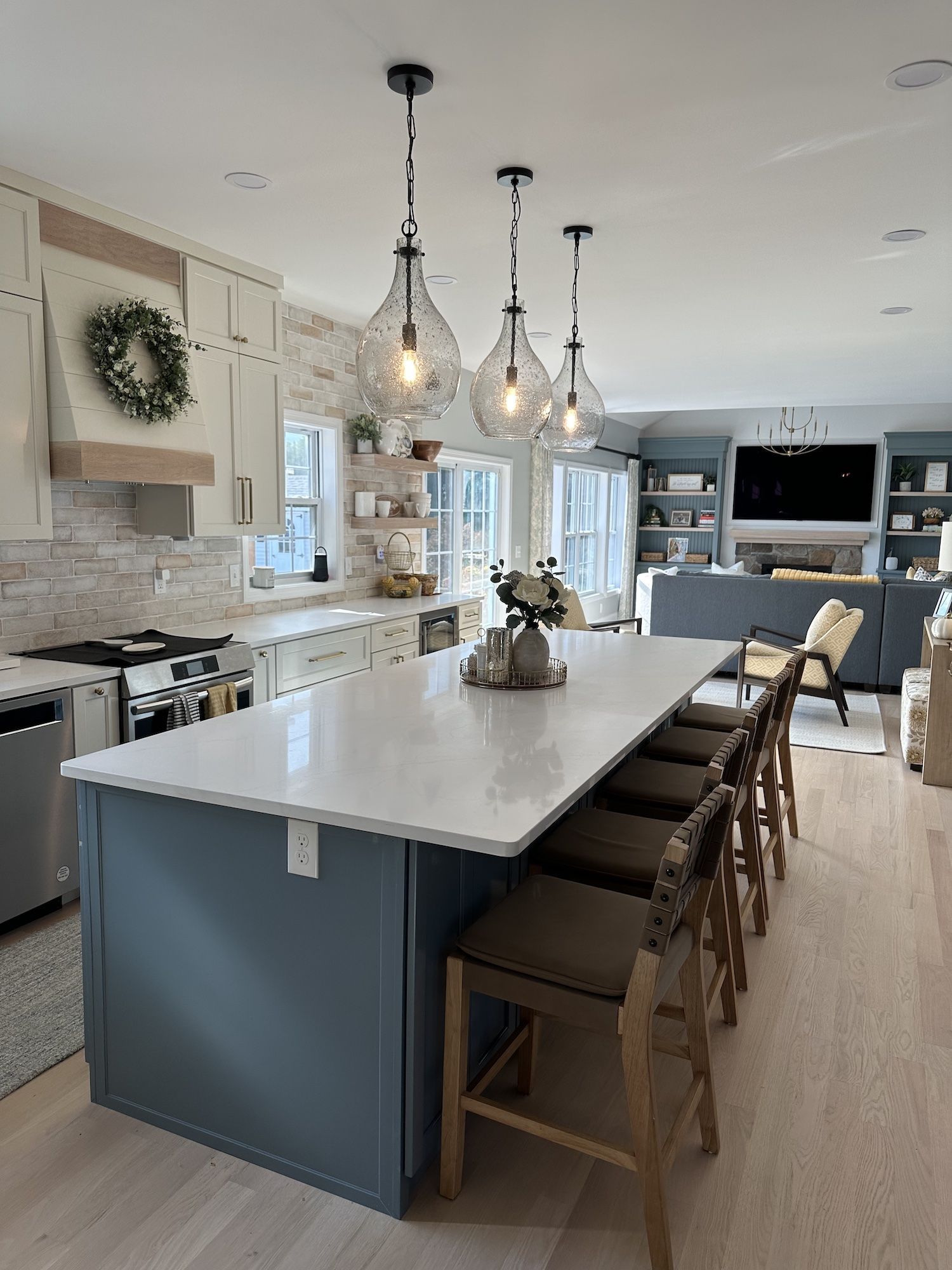 Spacious kitchen with a blue island, white countertops, pendant lights, and bar stools. Living room in the background.