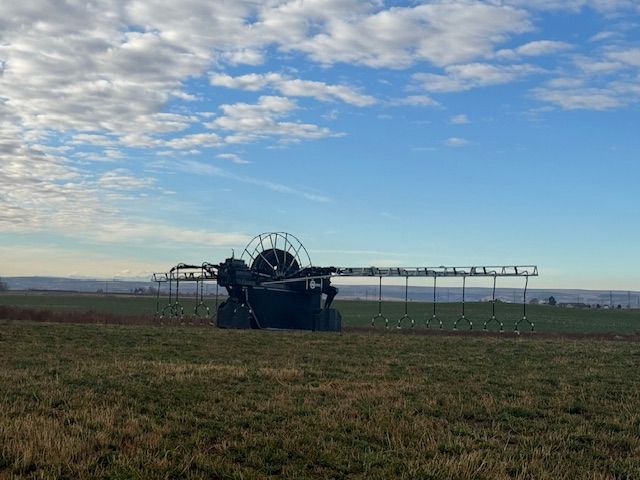 Large agricultural sprayer in a green field under a blue sky with clouds.