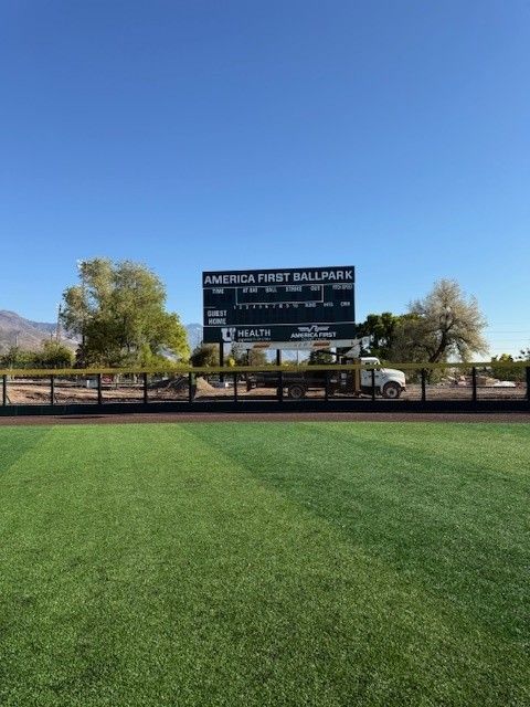 Baseball field with green grass, scoreboard, and blue sky.