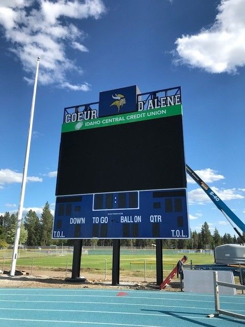 Large electronic scoreboard at Coeur d'Alene High School, blue and green, on a track with a clear sky in the background.