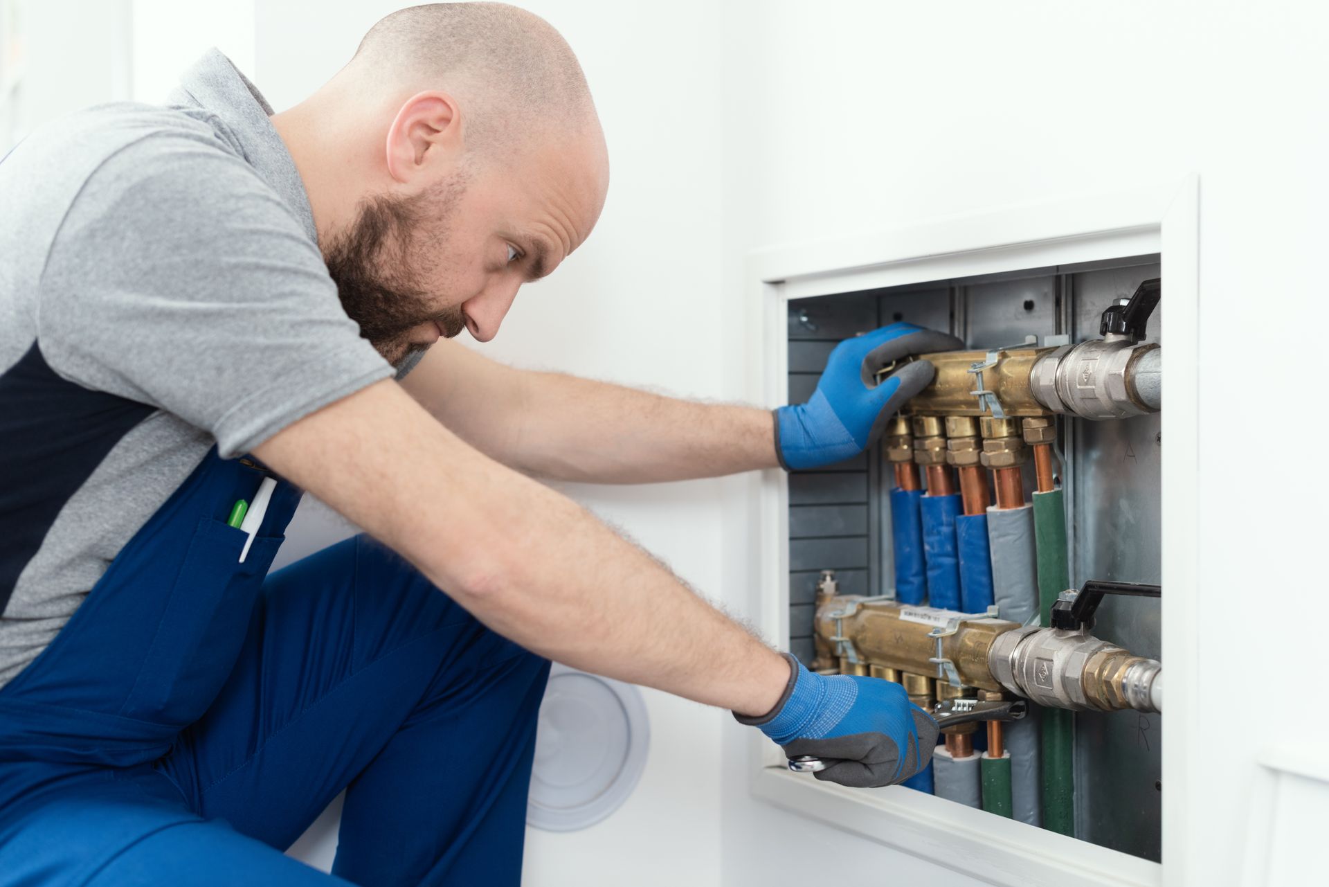 Technician using a wrench to adjust valves on indoor plumbing manifold system.
